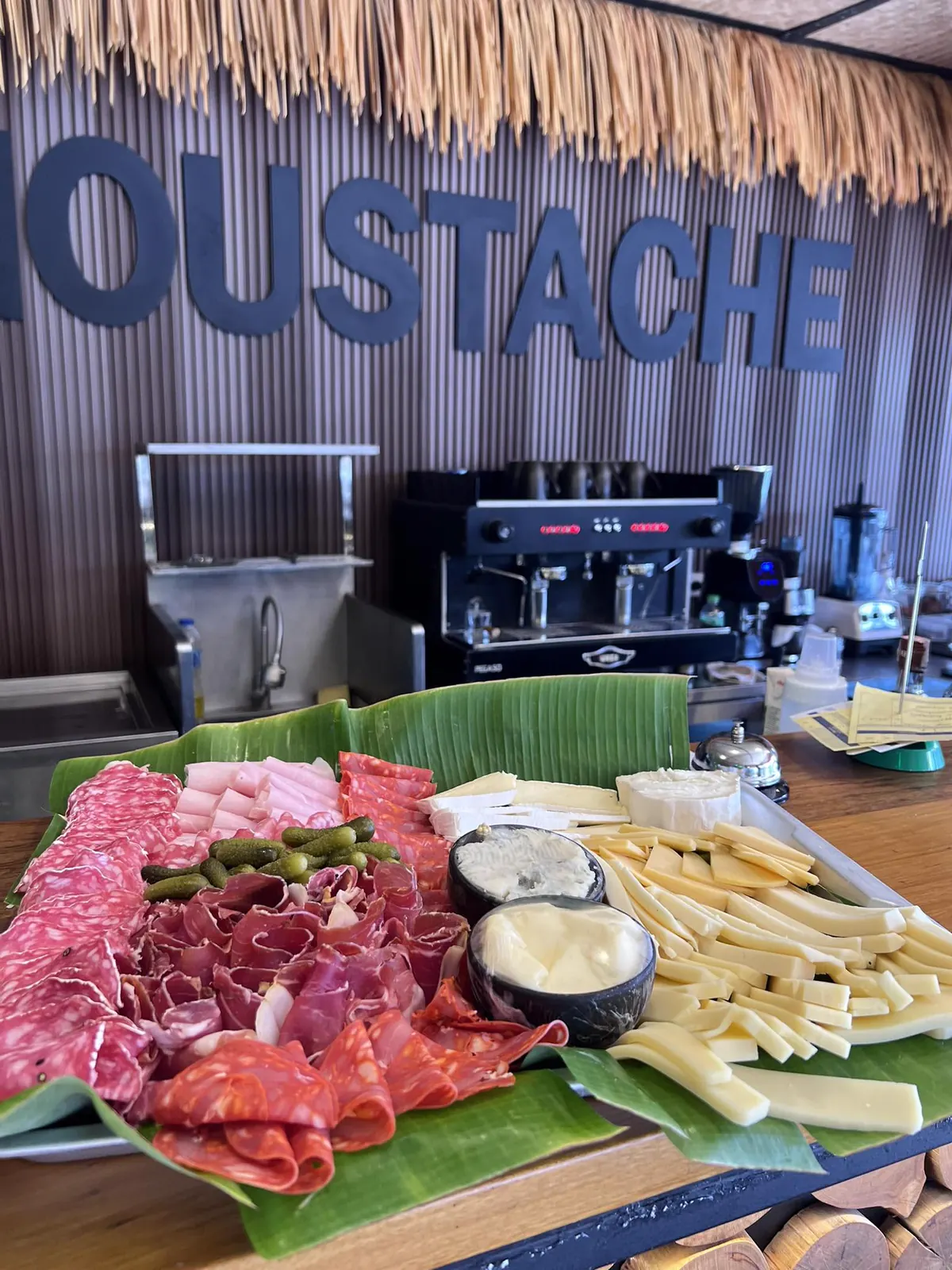 French charcuterie and cheese board on banana leaf in front of the Moustache sign