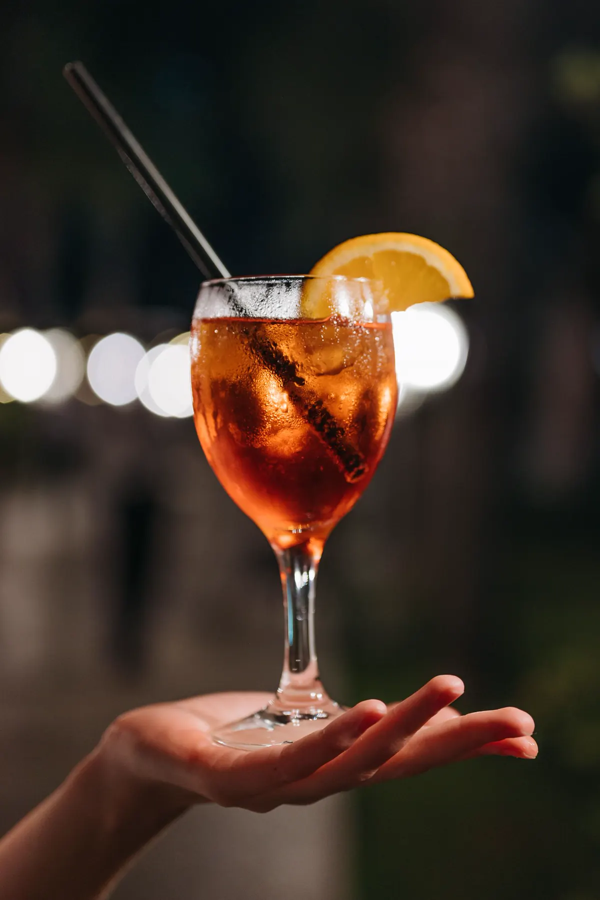 Aperol spritz held up against evening lights